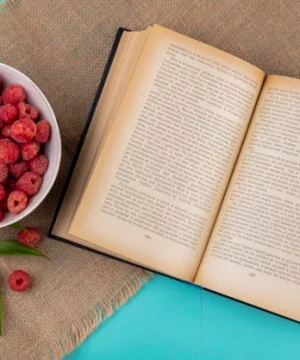 top-view-raspberries-bowl-open-book-with-leaves-sackcloth-blue-surface_141793-16139