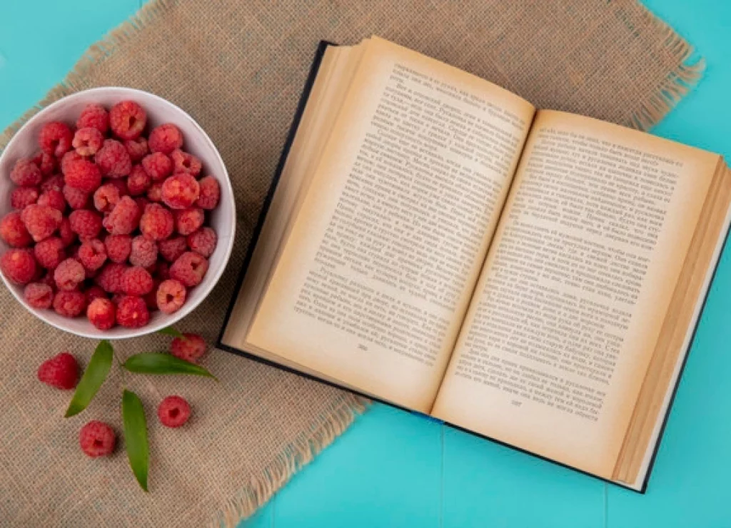 top-view-raspberries-bowl-open-book-with-leaves-sackcloth-blue-surface_141793-16139